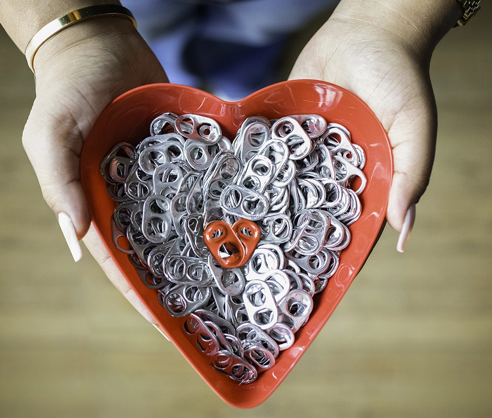 hands holding a heart shaped bowl filled with pop tabs